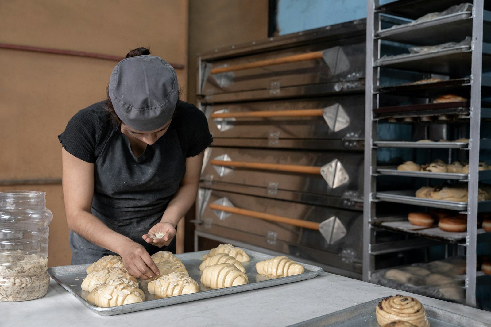 A young Hispanic baker is covering croissants with almond toppings before baking